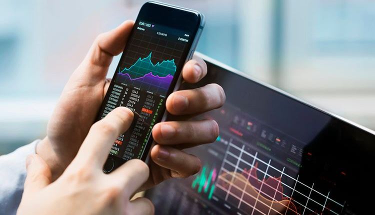 Trader analysing live forex and stock charts on a smartphone and tablet in the United Kingdom